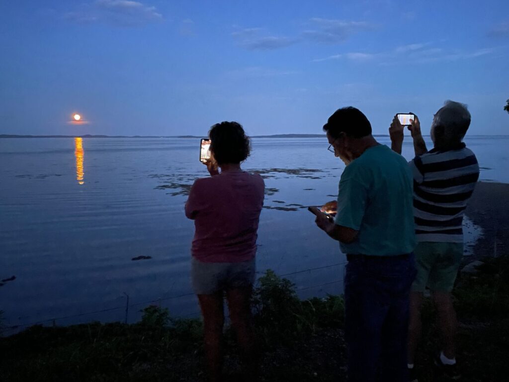People taking pictures of the full moon over the water