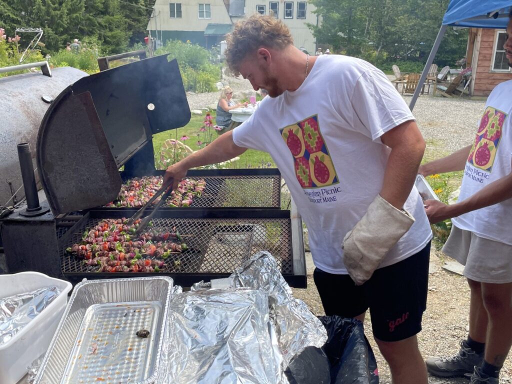 man cooking shish kebab on wood fired grill